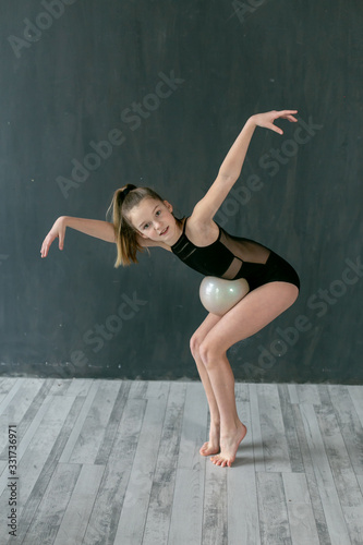 vertical portrait of a little gymnast performing an exercise with a ball on a light gray floor