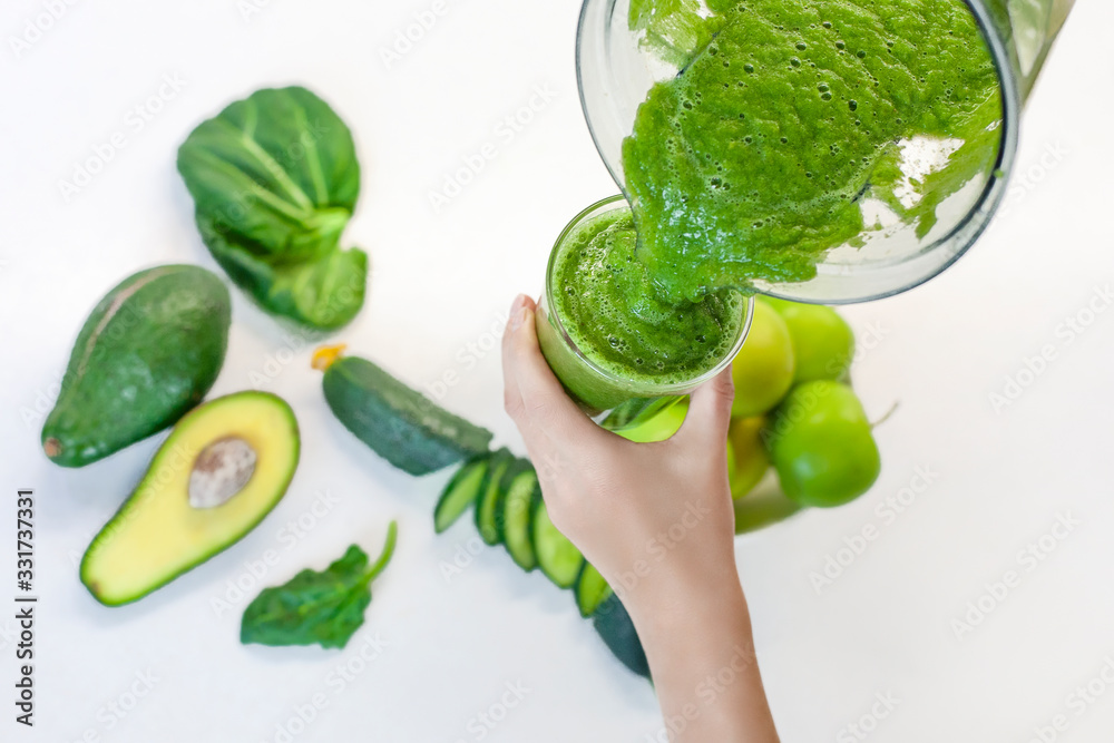 Woman pours green smoothie from a blender into a glass. Girl makes a healthy smoothie from a green apple and spinach. Morning detox for a healthy lifestyle, weight loss, ketone diet, raw food diet Woman pours green smoothie from a blender into a glass. Girl makes a healthy smoothie from a green apple and spinach. Morning detox for a healthy lifestyle, weight loss, ketone diet, raw food diet