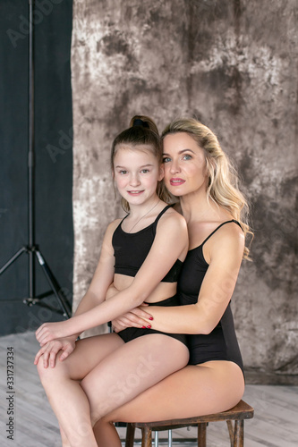 vertical portrait on a gray background of a young pretty European with a ten-year-old daughter