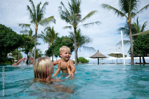 Happy infant baby boy enjoying his first swim in pool