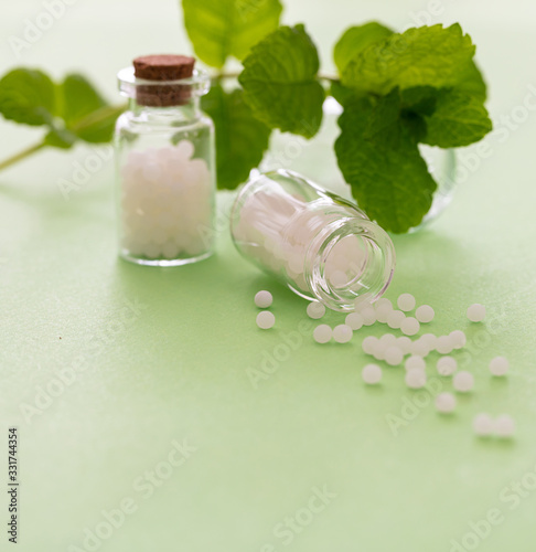 Homeopathy, globules scattered out of glass bottle, green background