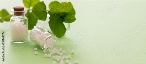 Homeopathy, globules scattered out of glass bottle, green background photo