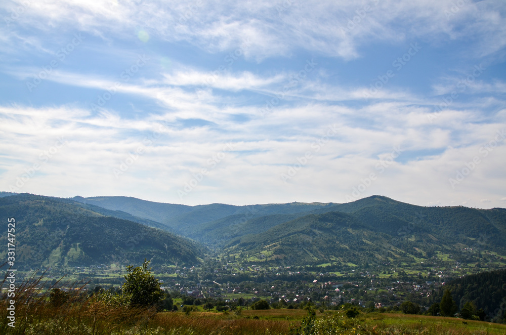 Beautiful sky and forest high up in Carpathian mountains. Village on a mountain hill, covered with fresh green grass
