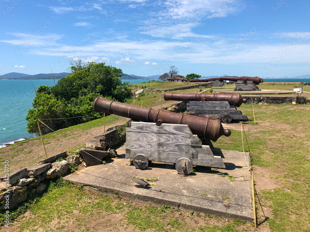 Santa Cruz de Anhatomirim Fortress. view from land to the ocean. on the island there are cannon, fences, viewing platforms and a lighthouse Santa Cruz de Anhatomirim Fortress. view from land to the ocean. on the island there are cannon, fences, viewing platforms and a lighthouse