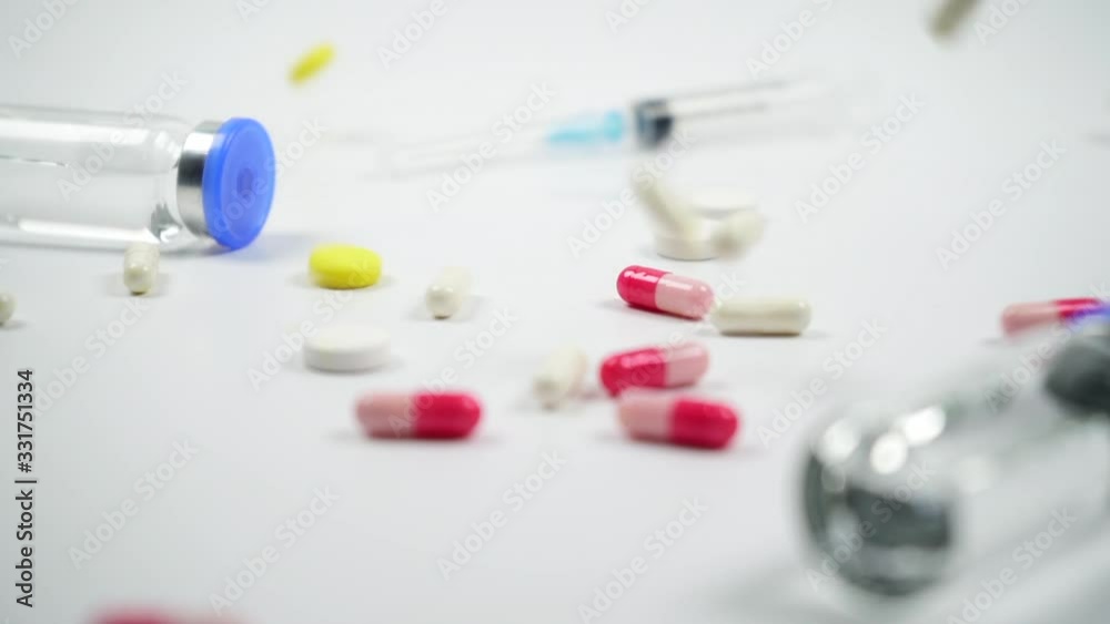 Colored pills falling in slow motion. Pills, medicine bottles, syringe on white background. Camera moves Colored pills falling in slow motion. Pills, medicine bottles, syringe on white background. Camera moves