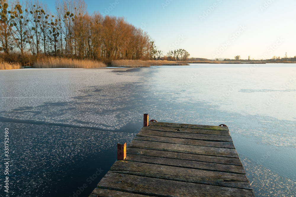 Wooden jetty and frozen lake, sunny day