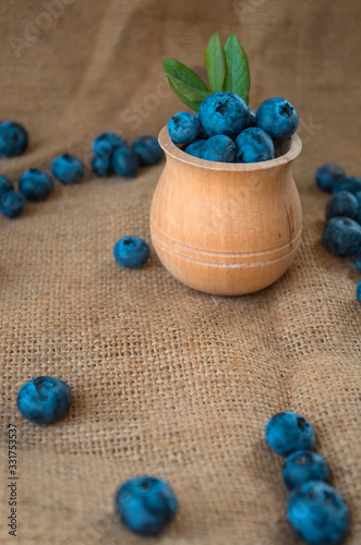 Fresh organic blueberries in a wooden bowl on a sackcloth background. Juicy and fresh blueberries with green leaves on rustic table. Bilberry on wooden Background. Blueberry antioxidant
