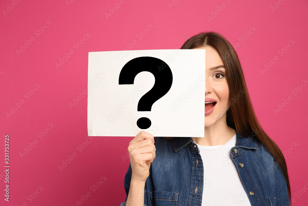 Emotional woman holding question mark sign on pink background Emotional woman holding question mark sign on pink background