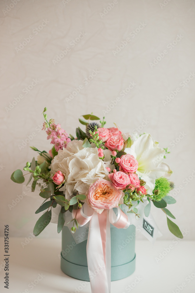 A large flower arrangement in a hat box was created by a florist for a wedding gift. Hydrangea, amarallis, roses and eucalyptus in a bouquet