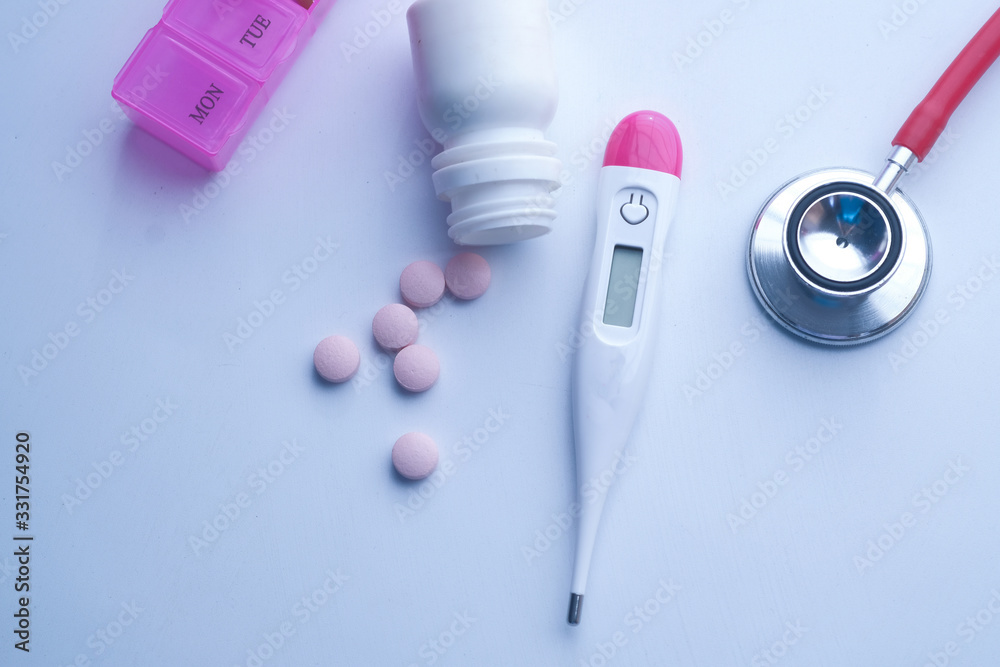 close up of stethoscope, pills and thermometer on pink background 