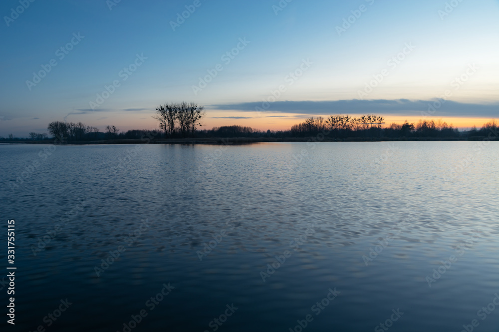 Calm water, trees on the horizon and the sky after sunset
