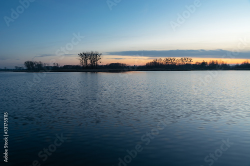 Calm water, trees on the horizon and the sky after sunset