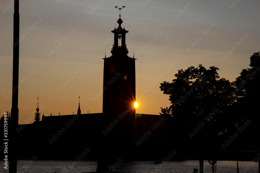 A sun flare is visible just behind the Stockholm City Hall as the sun sets on a warm summer evening in the capital of Sweden. It gives a feeling of calm and hope.