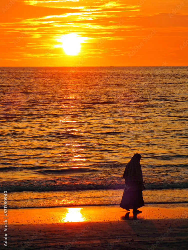 Silhouette of a muslim woman walking on a beach at sunset