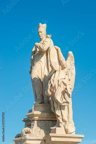Ancient statue of a monk with angel at the Charles Bridge in Prague at blue sky, Czech Republic, summer, closeup
