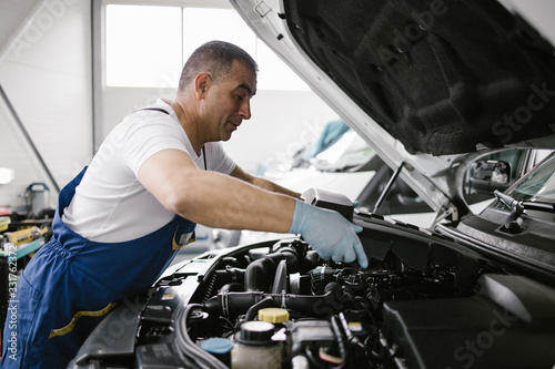 Car service mechanic worker standing in front of car engine open hood and working