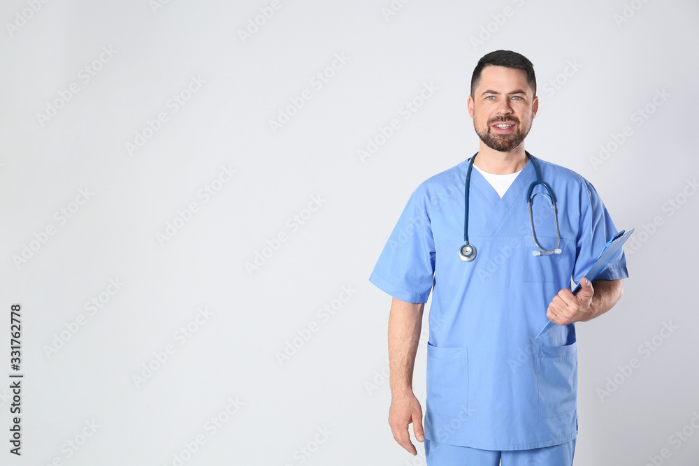 Portrait of mature doctor with clipboard against light background Portrait of mature doctor with clipboard against light background