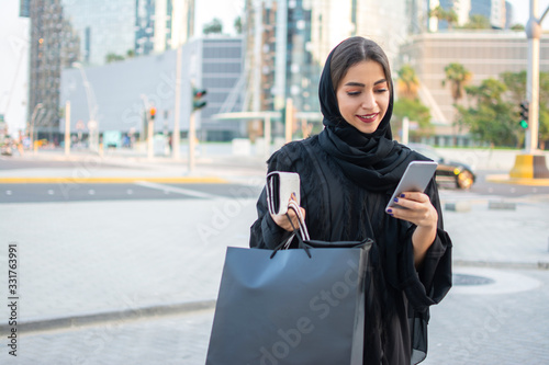 Beautiful muslim woman using phone while walking on street after shopping photo