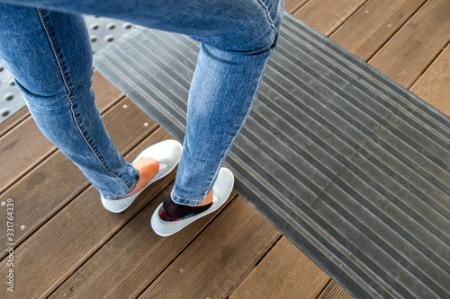 Female legs in denim jeans pants and light summer sneakers standing on wooden floow.