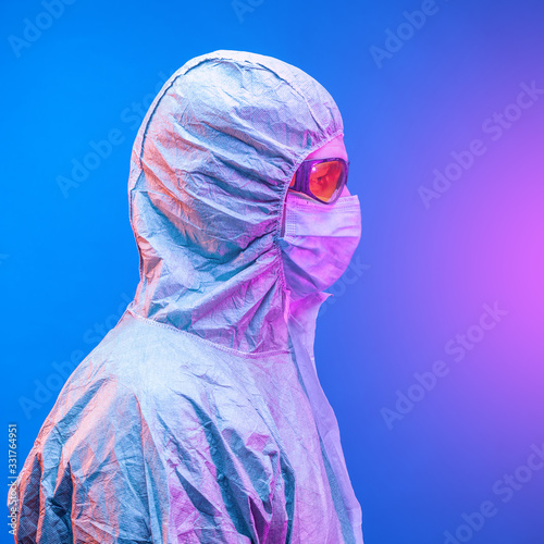 A chemist in a green protective suit , mask and yellow glasses protects himself from a bright flash