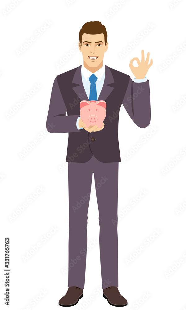Smiling Businessman holding a piggy bank and showing a okay hand sign. Full length portrait of Businessman in a flat style. Smiling Businessman holding a piggy bank and showing a okay hand sign. Full length portrait of Businessman in a flat style.