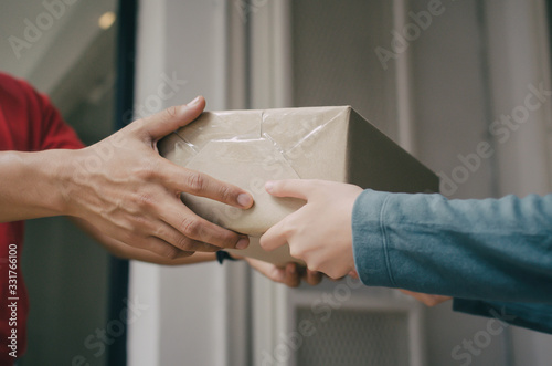 hand of delivery service man in red uniform with woman customer receiving parcel post box from courier at home, cargo shipping, fast express delivery service, online shopping and logistic concept