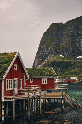 traditional red fishing hut whit grass roof in reine lofoten  with sea and mounatin view