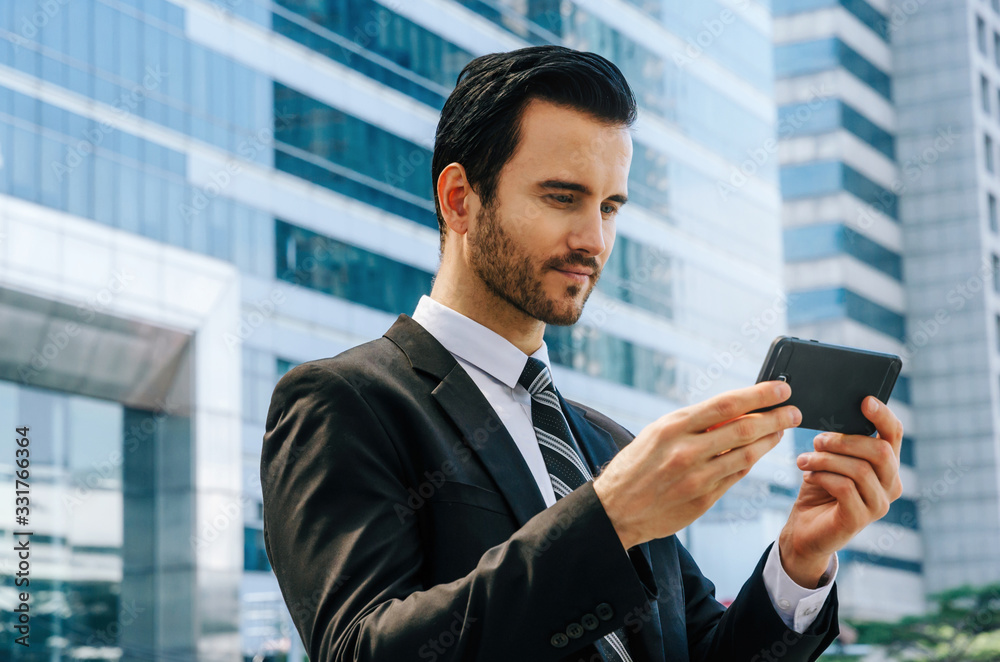 young smart caucasian business man wearing suit using mobile smart phone reading information about finance news with building city background, digital network technology, internet and business concept young smart caucasian business man wearing suit using mobile smart phone reading information about finance news with building city background, digital network technology, internet and business concept