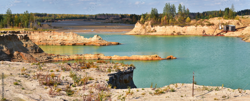 Turquoise water in deep steep sand quarries. Autumn panorama of industrial developments