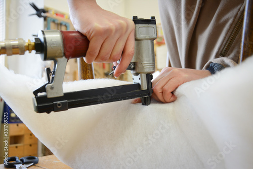 Making new upholstery on old restored furniture. Woman work with pneumatic stapler in upholstery workshop. 