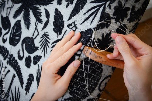 Upholstery workshop. Upholstery working process. Restoring old chair upholstery. Woman hands working. Hand sewing. Curved sewing needle.