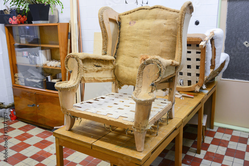 Making new upholstery on old chair inside upholstery workshop. Old armchair without upholstery. Working process, traditional hand work.