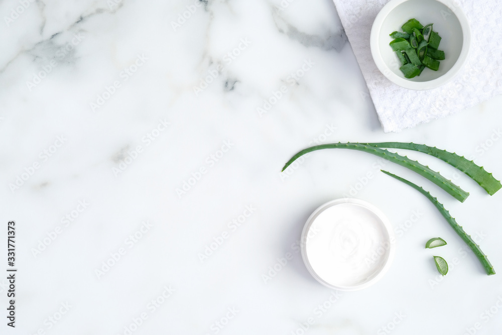 Natural organic SPA cosmetic jar and sliced stems aloe vera on marble background. Flat lay, top view. Beauty product for skin care concept.
