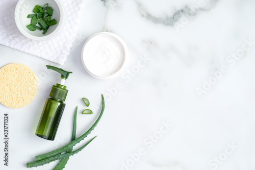 Natural organic SPA cosmetic lotion bottle, sponge and sliced stems aloe vera on marble background. Flat lay, top view. Skin care and beauty treatment concept.