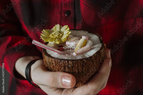 Female hand holding a coconut cocktail with berries and flower