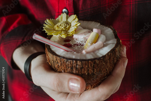 Female hand holding a coconut cocktail with berries and flower