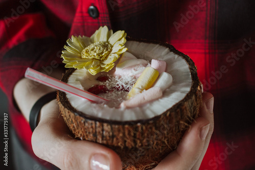 Female hand holding a coconut cocktail with berries and flower