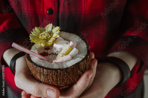 Female hand holding a coconut cocktail with berries and flower