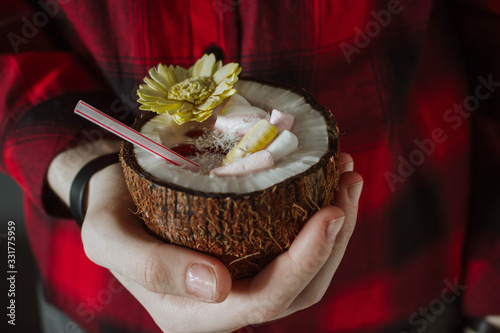 Female hand holding a coconut cocktail with berries and flower