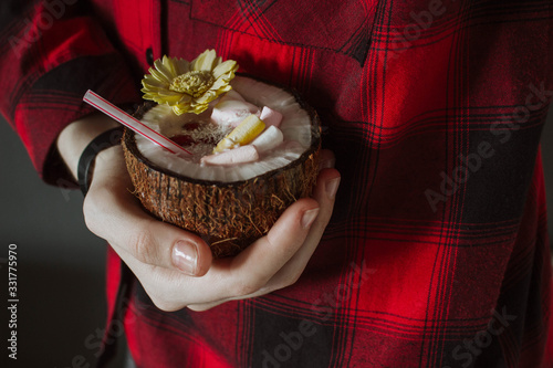 Female hand holding a coconut cocktail with berries and flower