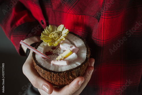 Female hand holding a coconut cocktail with berries and flower