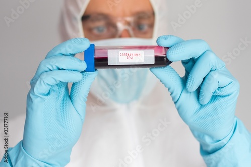 Scientist in protective suit holding test tube with blood