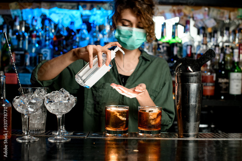 girl bartender in medical mask treats her hands with disinfector