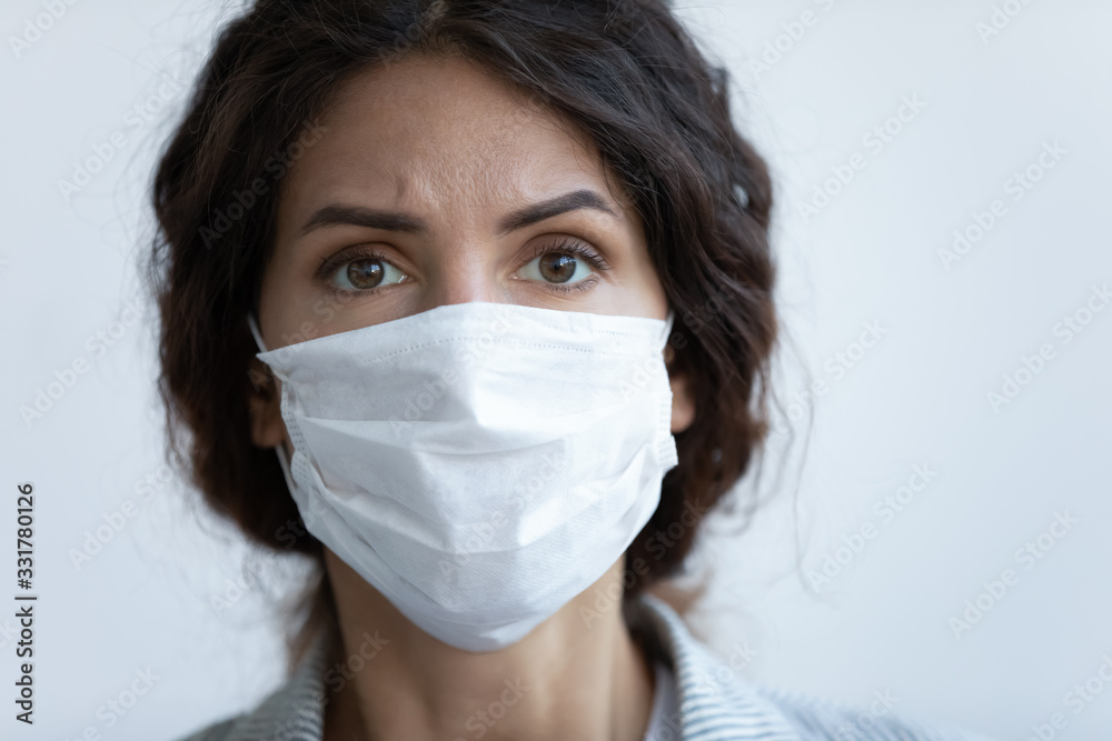 Close up front view concerned woman face portrait wear facial mask pose on blue studio background look at camera feels afraid. COVID-19 sars-cov-2 epidemic pandemic virus outbreak protection concept Close up front view concerned woman face portrait wear facial mask pose on blue studio background look at camera feels afraid. COVID-19 sars-cov-2 epidemic pandemic virus outbreak protection concept