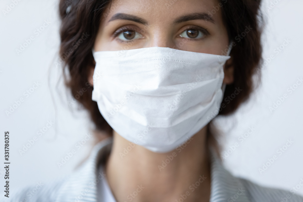 Close up portrait of beautiful 30s young millennial woman cover her face wearing facial medical blue mask, anti-coronavirus COVID-19 pandemic infectious disease outbreak protection, healthcare concept