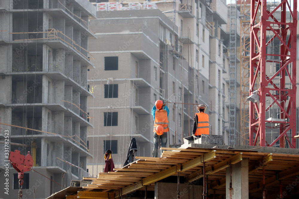 Builders work at the construction site, installation of formwork for walls. Workers on background of residential buildings under construction Builders work at the construction site, installation of formwork for walls. Workers on background of residential buildings under construction