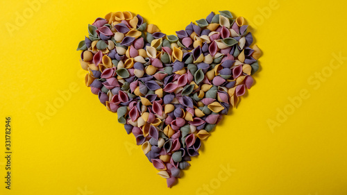 Heart of  Pasta Conchiglie Rigate, mix of colorful uncooked shells with spinach and tomatoes. Textured Italian food background concept. Top view flat lay close up copy space