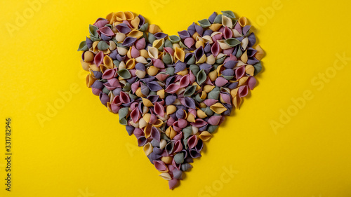 Heart of  Pasta Conchiglie Rigate  mix of colorful uncooked shells with spinach and tomatoes. Textured Italian food background concept. Top view flat lay close up copy space