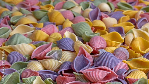 Pasta Conchiglie Rigate, mix of colorful uncooked shells with spinach and tomatoes. Textured Italian food background concept. Top view flat lay close up copy space photo