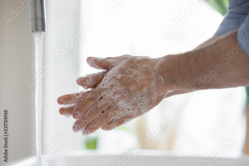 Water pour from tap while man wash his hands with anti bacterial soap close up view. Personal hygiene morning activity, safety precautions against COVID-19 pandemic infectious disease outbreak concept